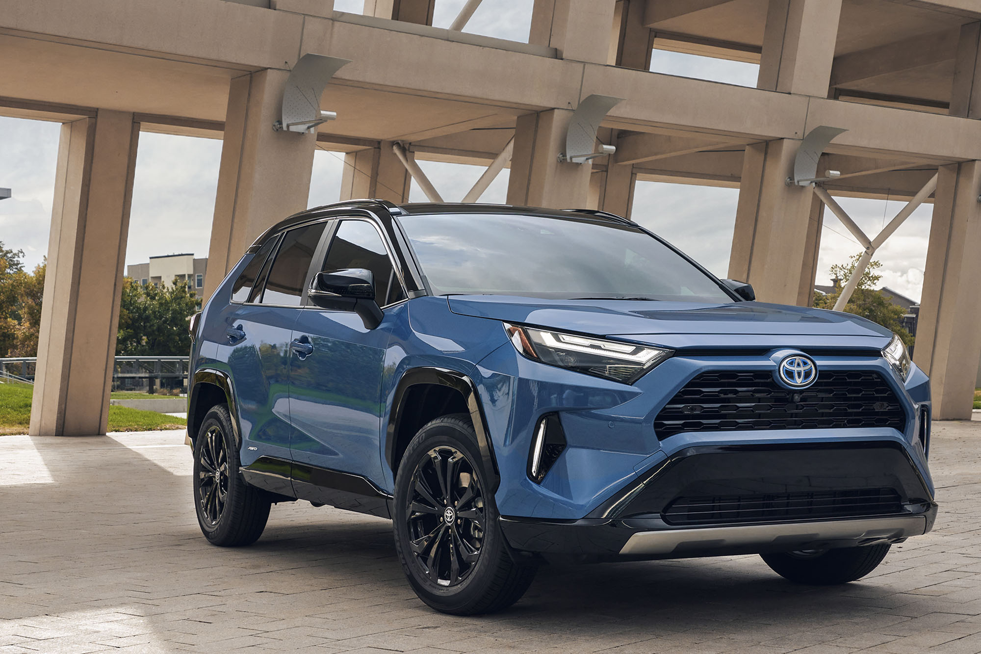 A front-right view of a blue Toyota RAV4 in front of modern architecture