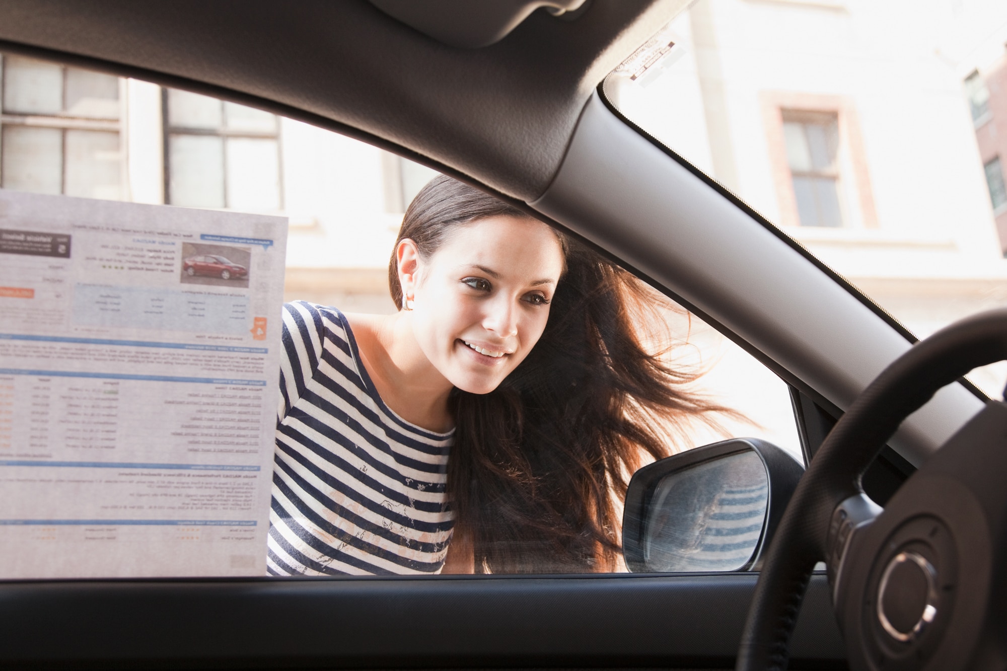 Woman staring into window of driver's seat of car she wants to buy with sticker of car details