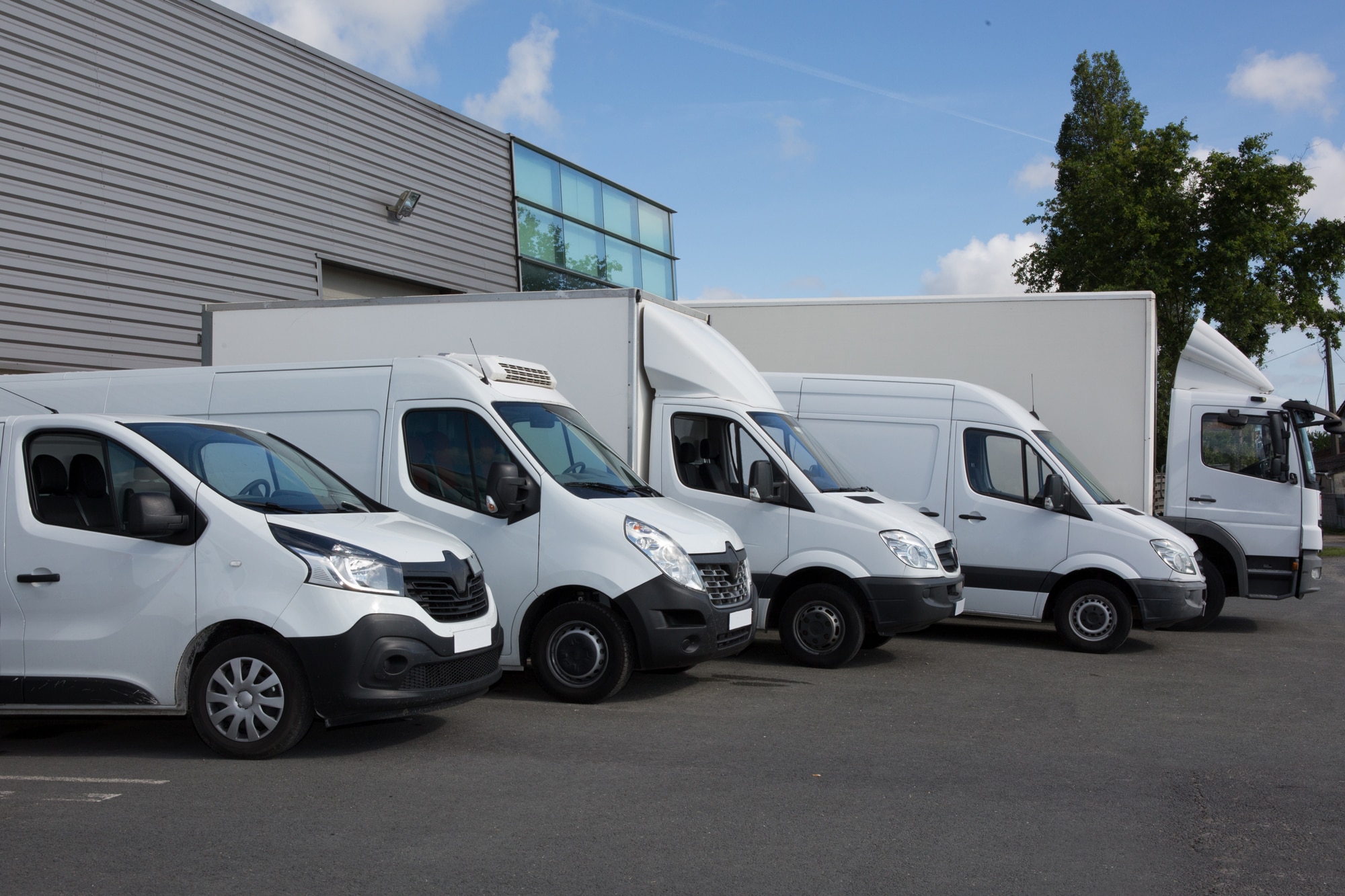 Fleet of white vans undefined trucks in different styles outside a business