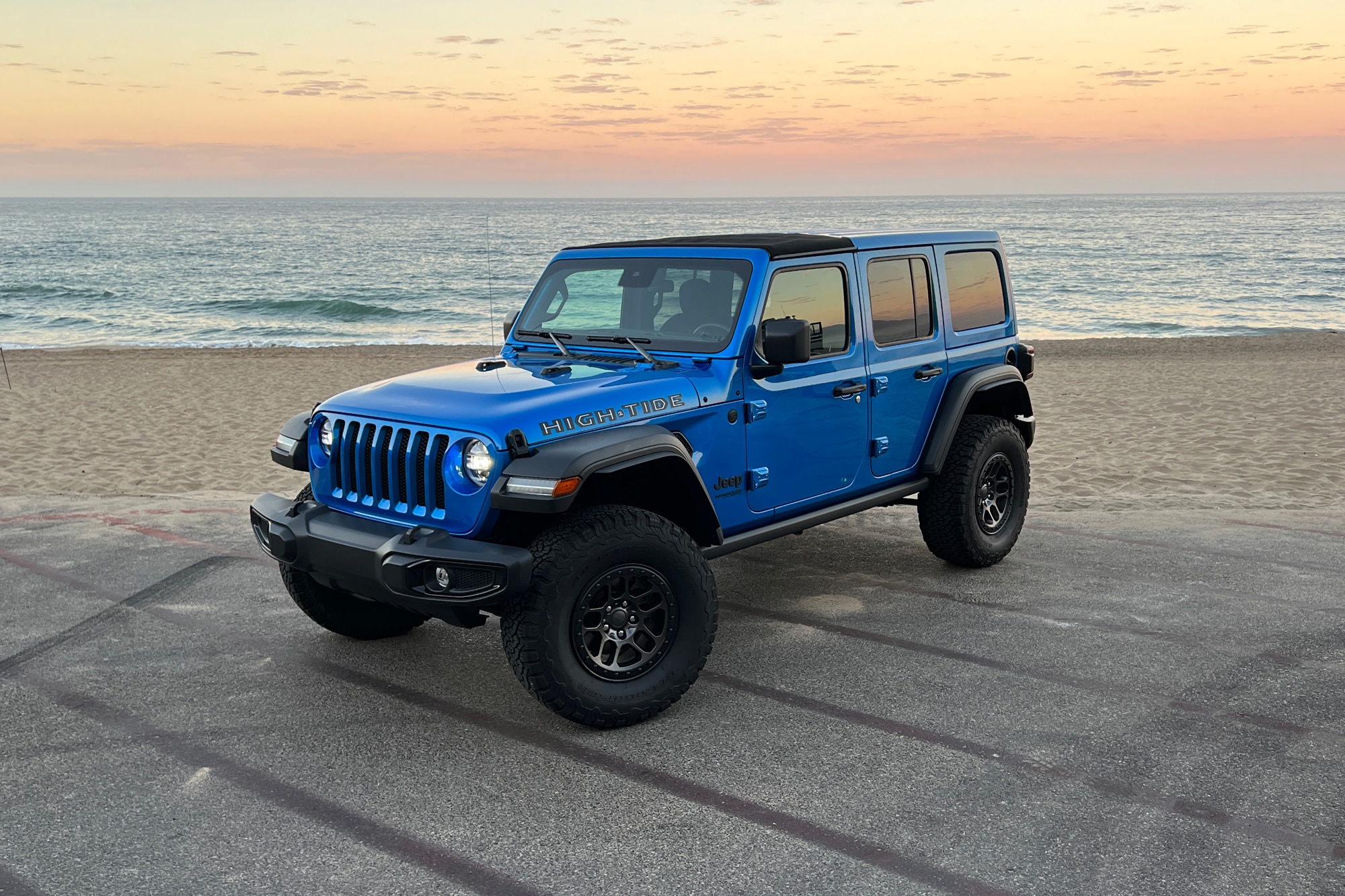 Blue 2022 Jeep Wrangler High Tide front quarter parked in front of sand and ocean
