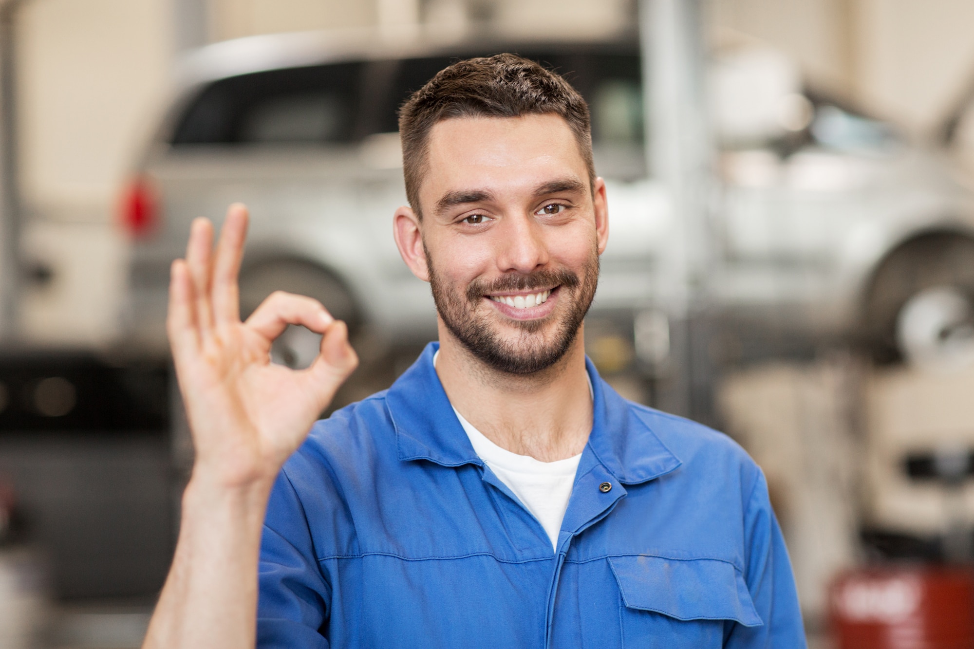 Mechanic in blue overalls smiling and giving all good sign with hand