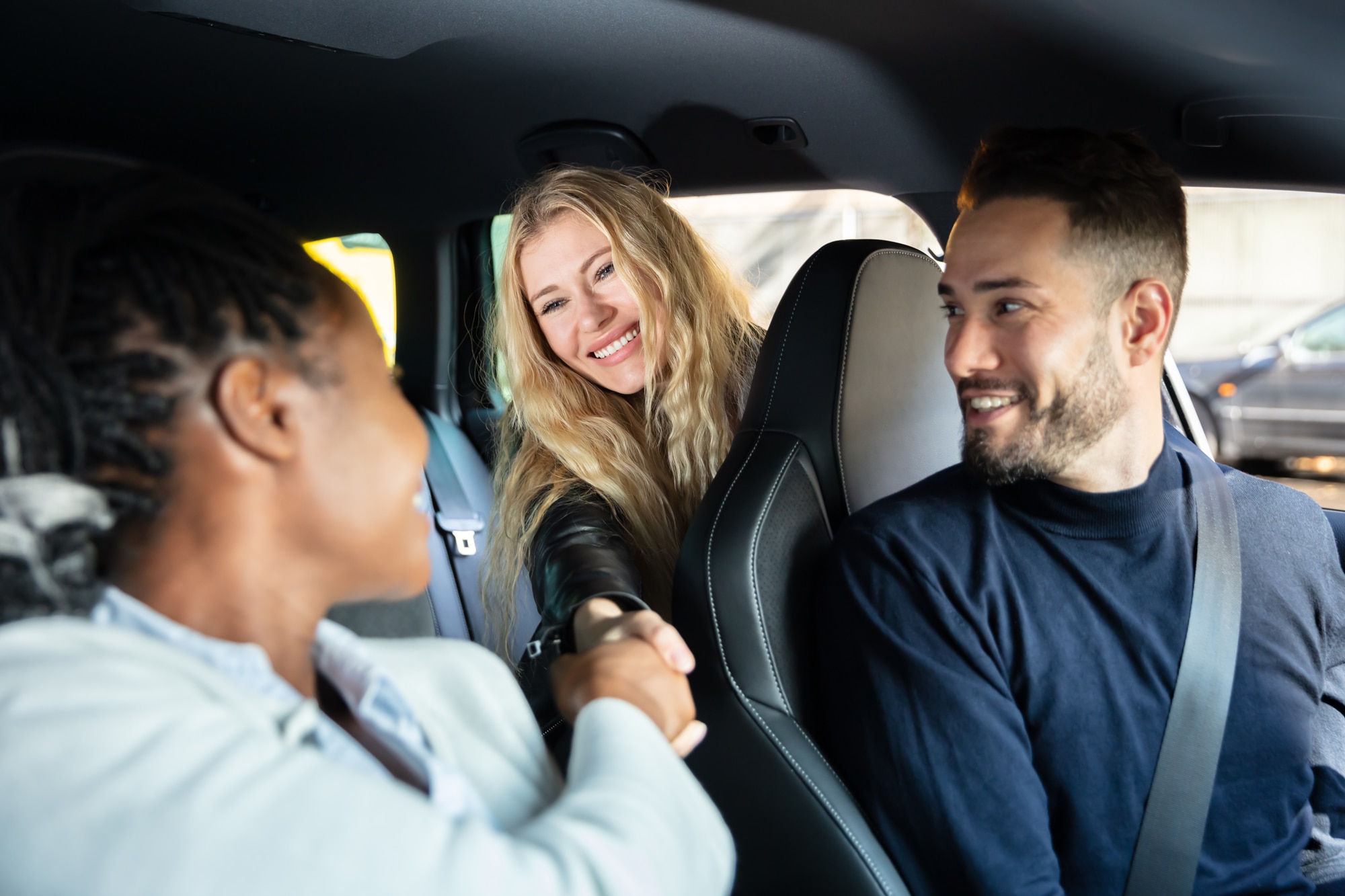 White man in driver's seat while black lady in front seat undefined white lady in the back shake hands