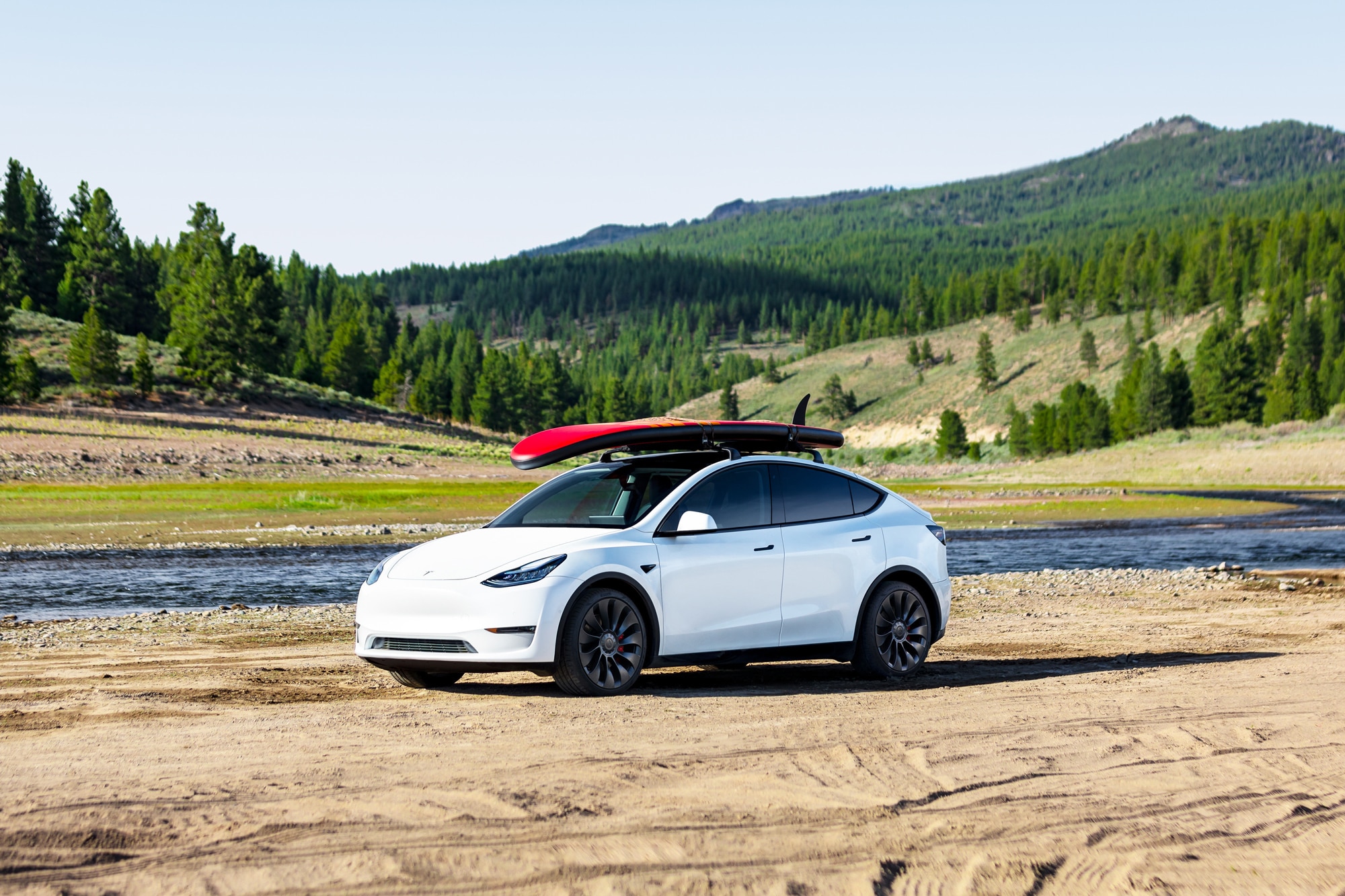 White Tesla Model Y with a surfboard parked by water