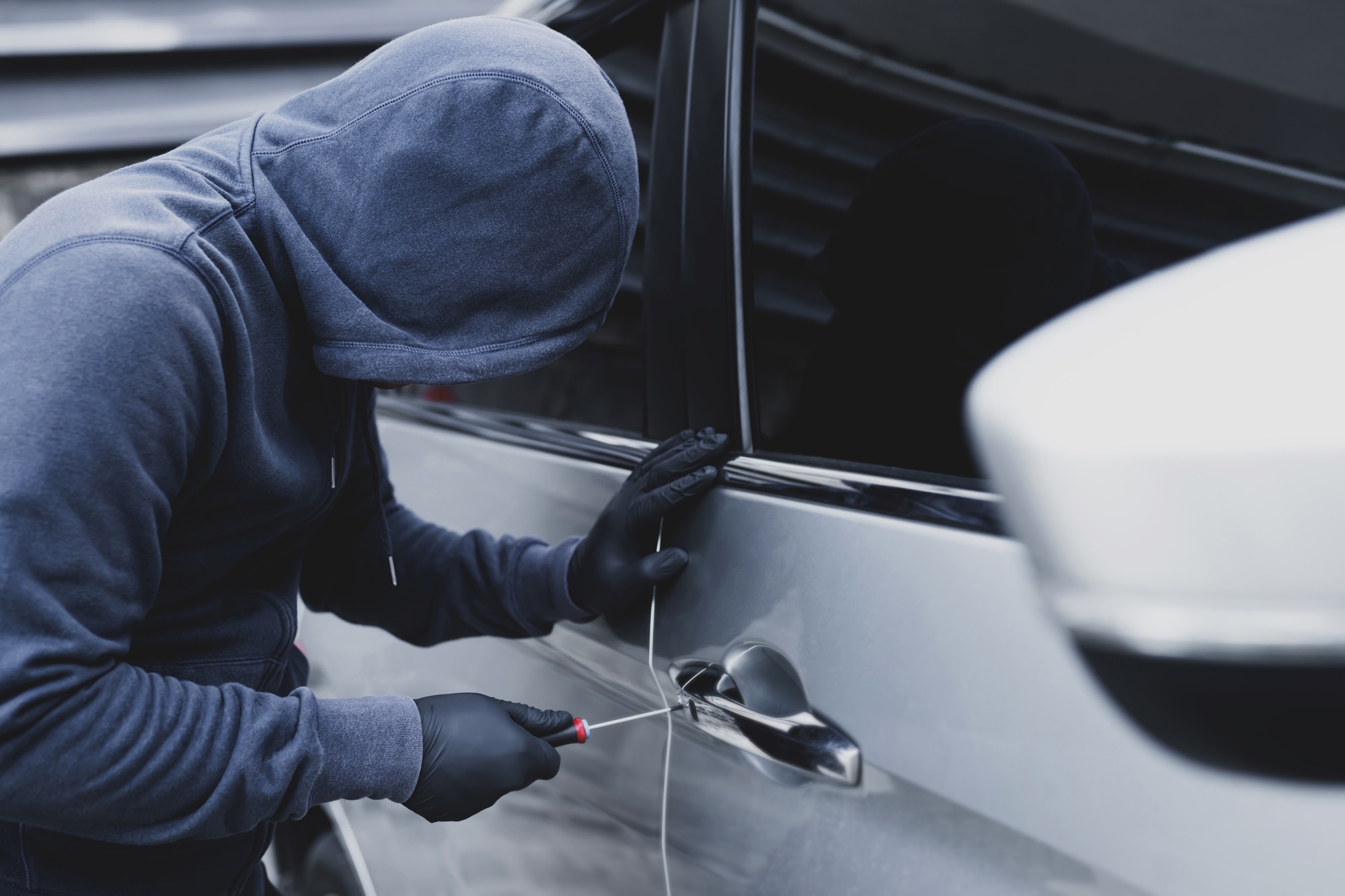 Hooded man trying to break into a car with a screwdriver