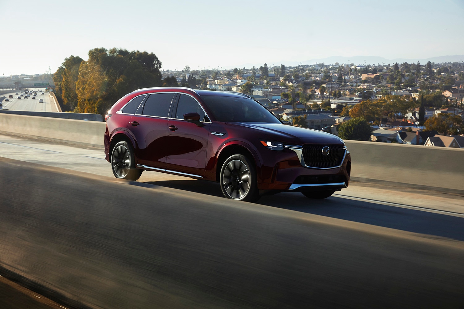 2024 Mazda CX-90 in dark red driving along a freeway overpass