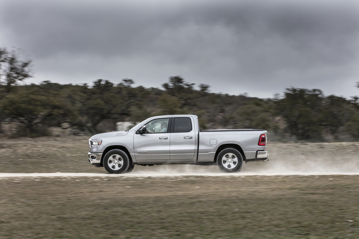  Profile shot of a 2023 Ram 1500 Big Horn Quad Cab in gray driving down a dirt road