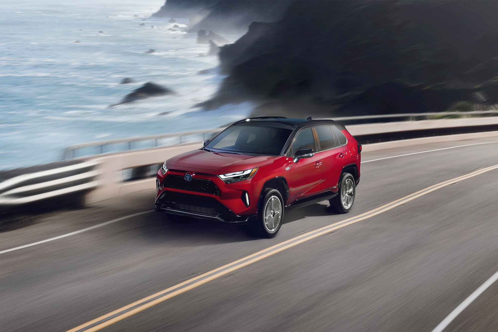 Red 2024 Toyota RAV4 Prime driving past the ocean on PCH