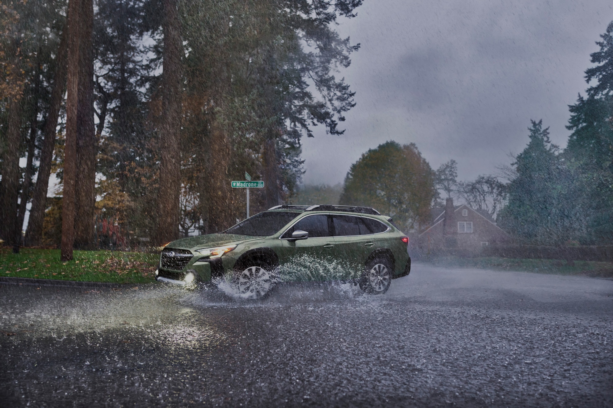 Green 2023 Subaru Outback driving in the rain at intersection