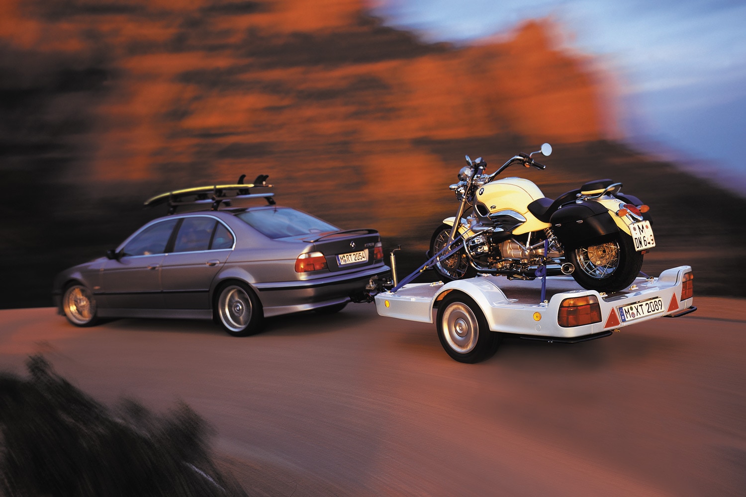 A blue BMW sedan tows a white trailer with a yellow BMW motorcycle.