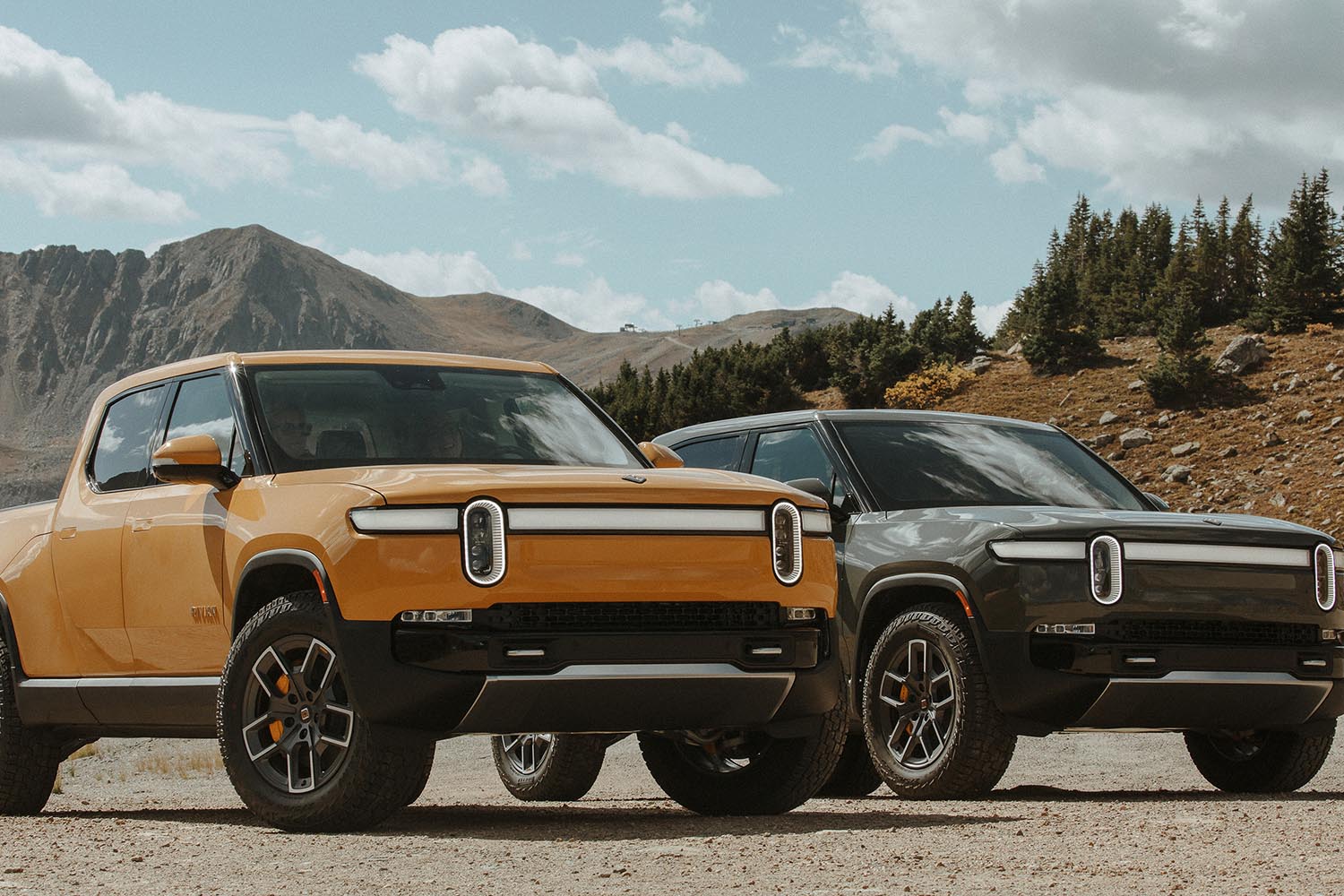 Two Rivian R1T trucks in orange and green parked on concrete