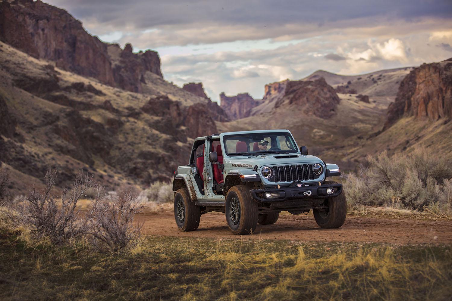 2024 Jeep Wrangler in blue driving along rugged, mountainous desert trail.