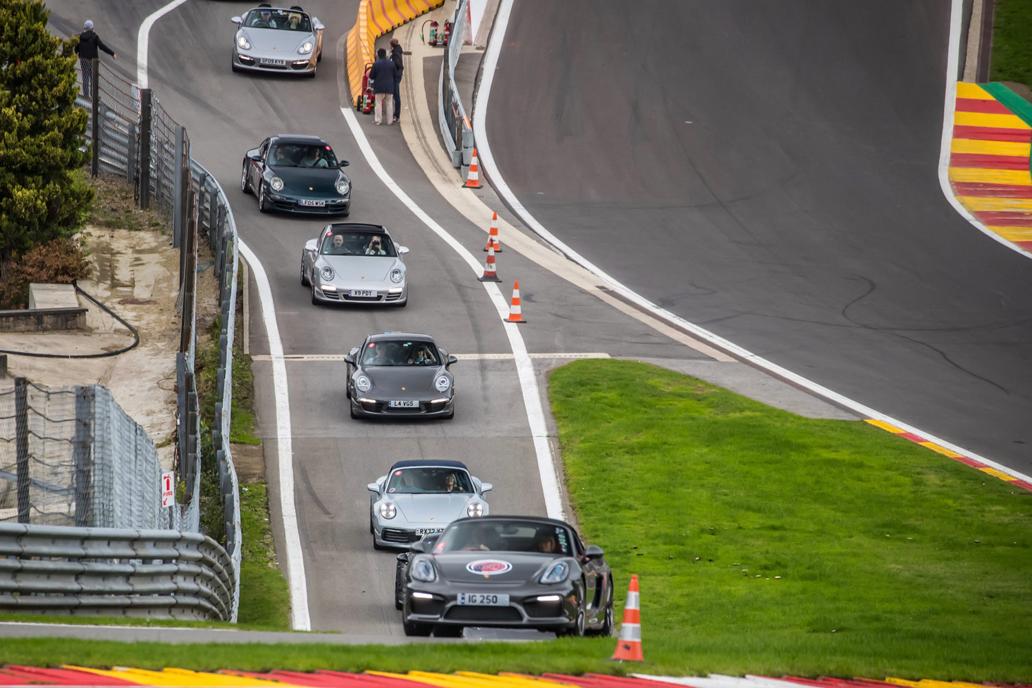 A group of six Porsches entering a racetrack.