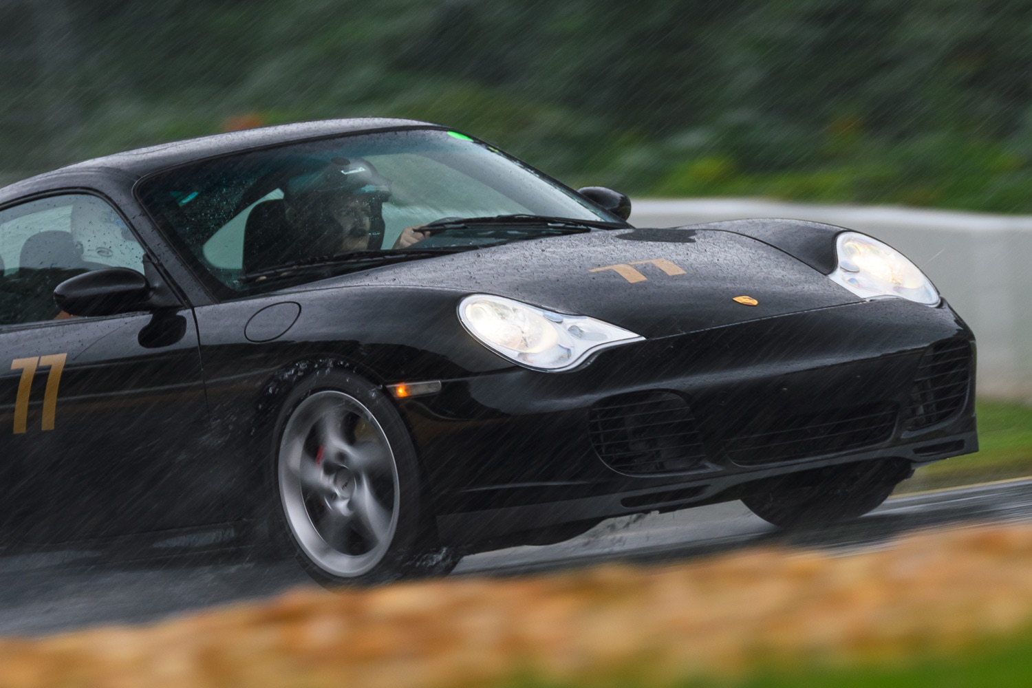 Person wearing a helmet driving a black Porsche in the rain.