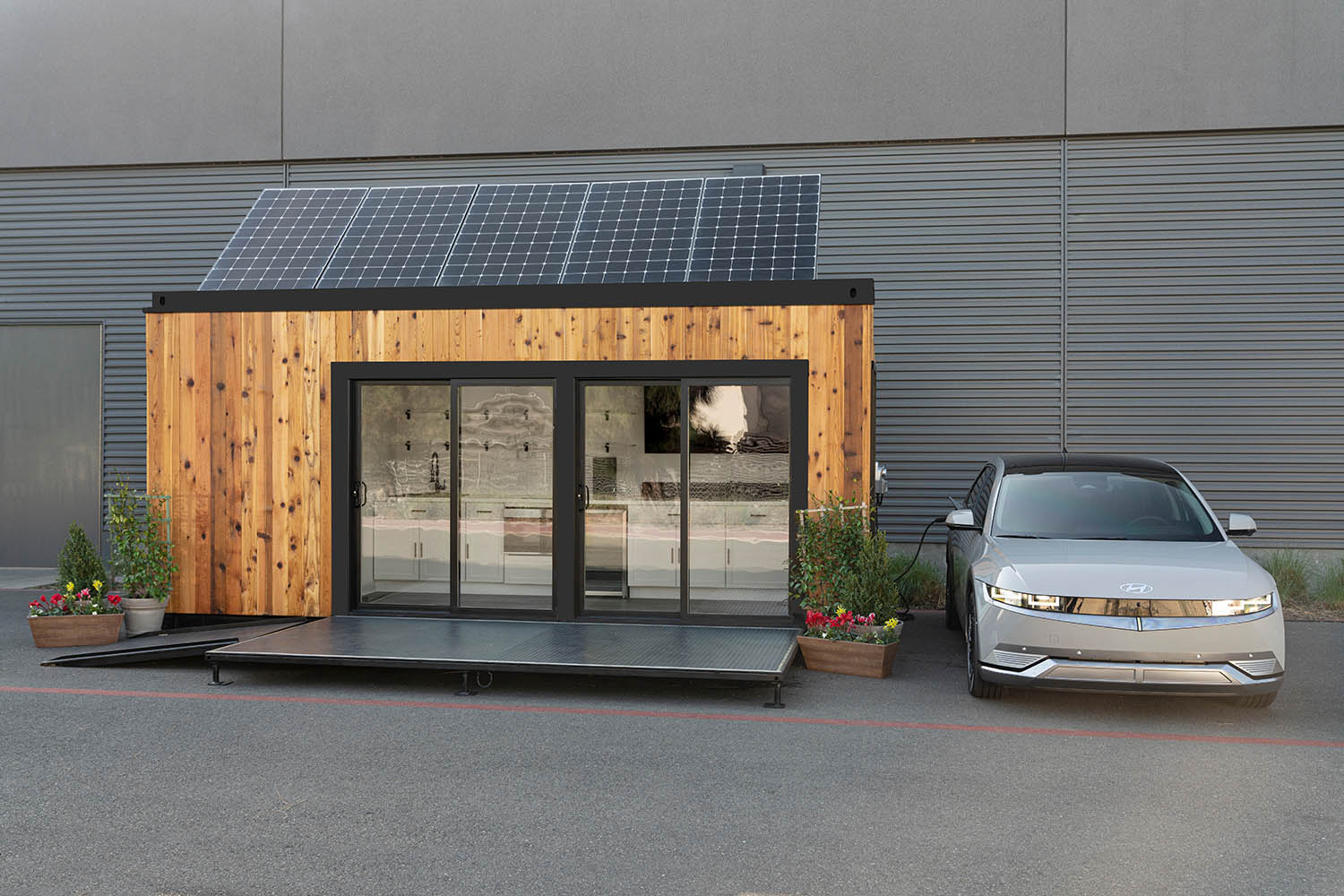 A gray Hyundai sedan plugged into a house equipped with rooftop solar panels.