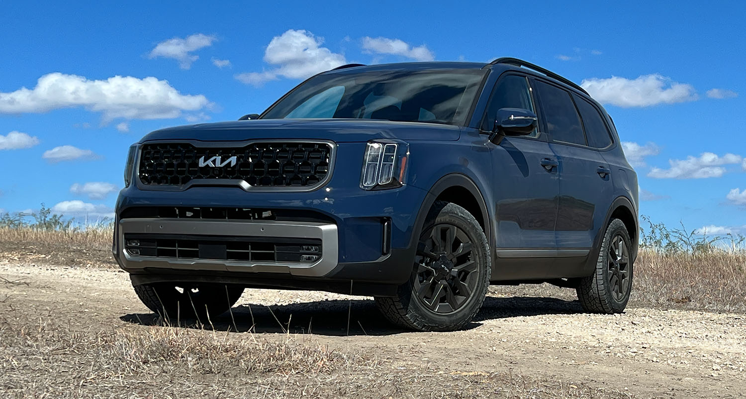 2023 Kia Telluride in blue parked on dirt, surrounded by dry brush.