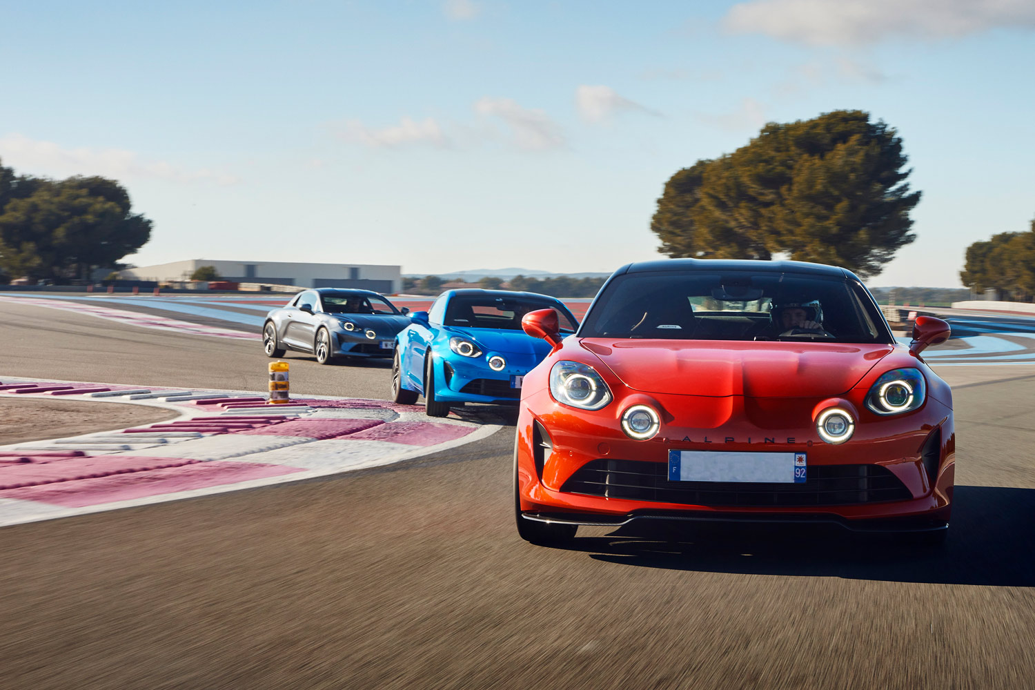 Three Alpine sports cars undefined red, blue, and gray undefined chase each other on a racetrack