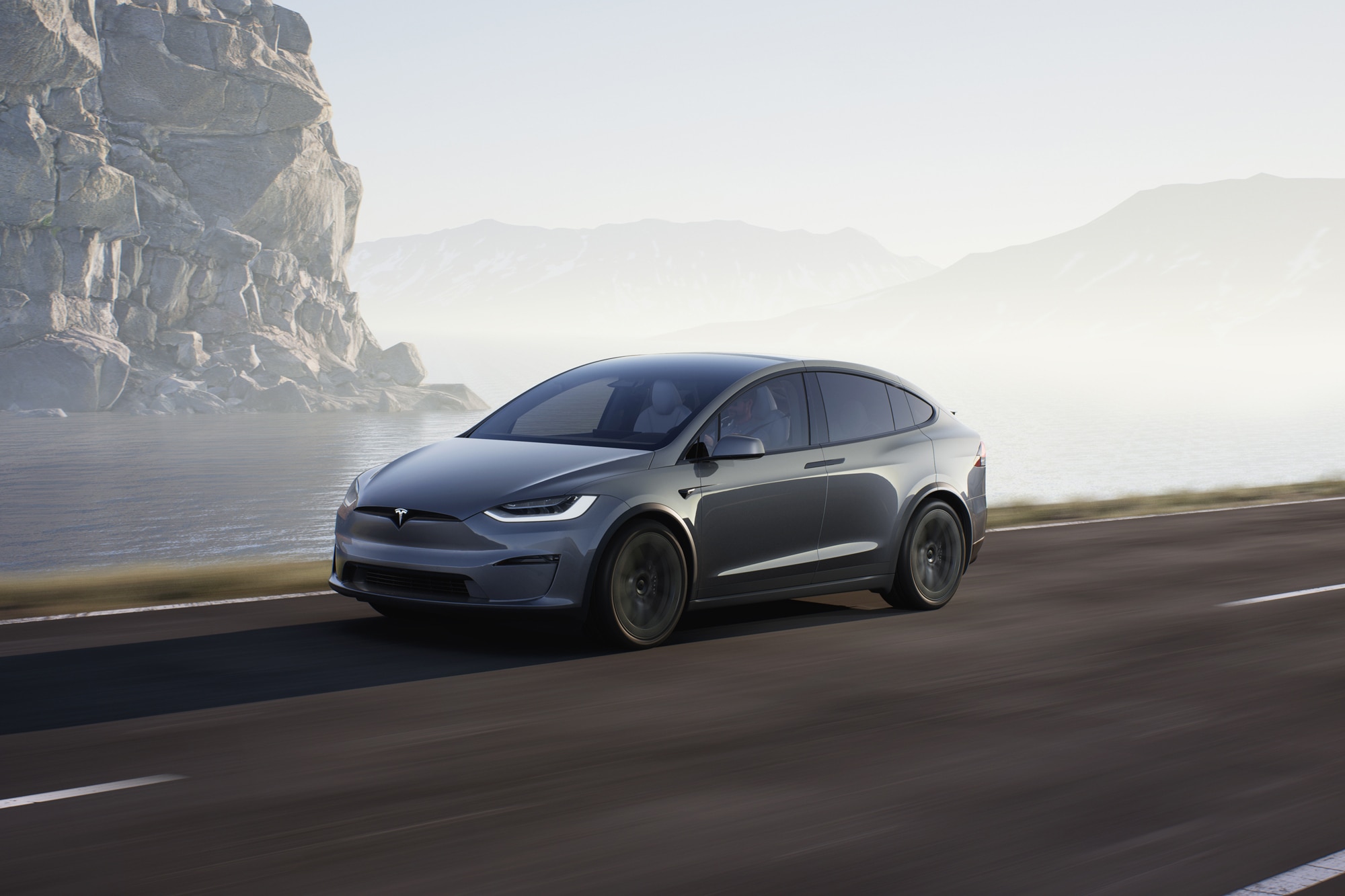 Gray 2022 Tesla Model X driving down highway next to water and mountains