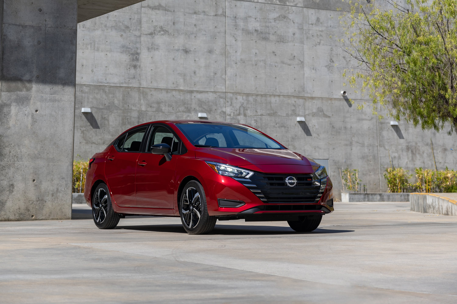 2023 Nissan Versa in red parked in front of concrete building.