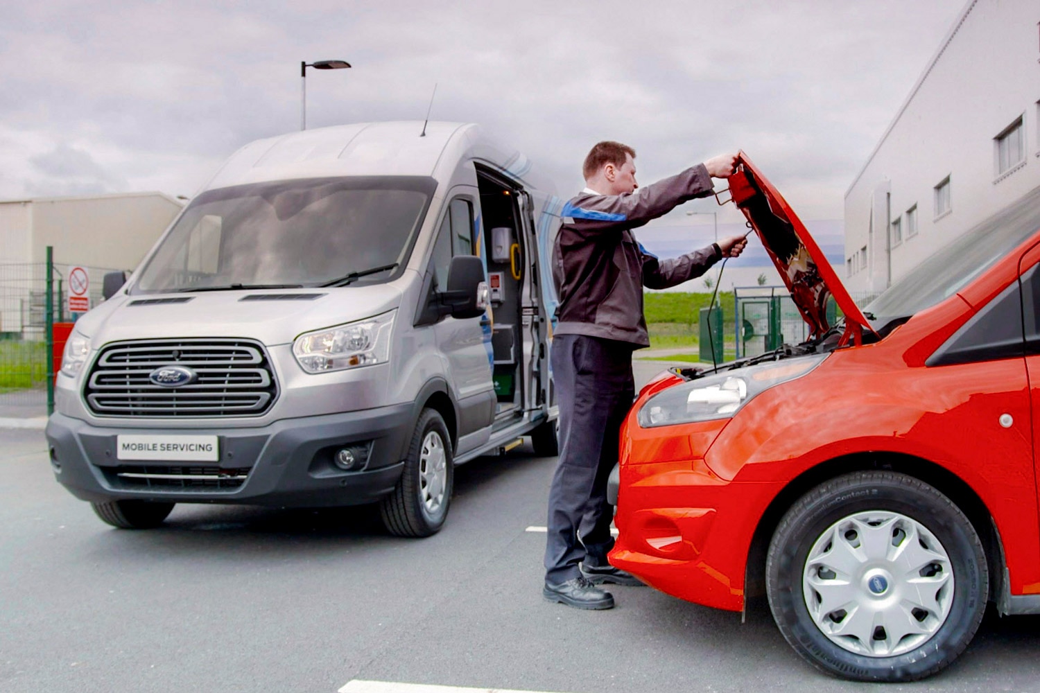 A Ford service tech opens the hood of a red Ford Transit Connect.
