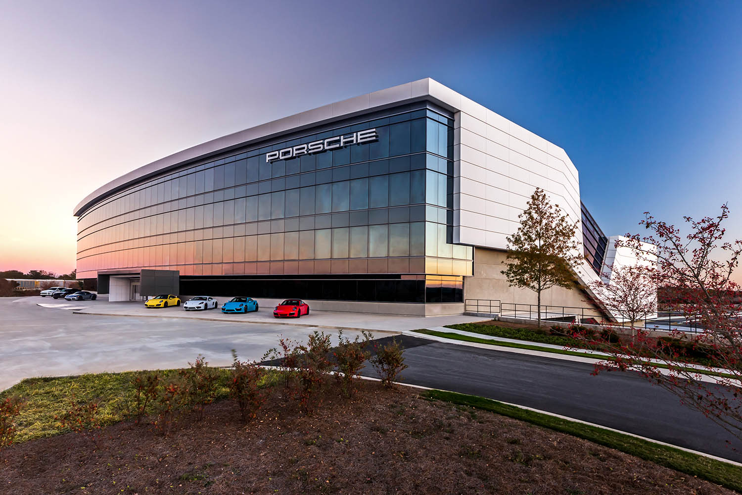 The front of Porsche's Experience Center in Atlanta, Georgia, with four Porsche sports cars parked outside, one each in yellow, silver, blue, and red