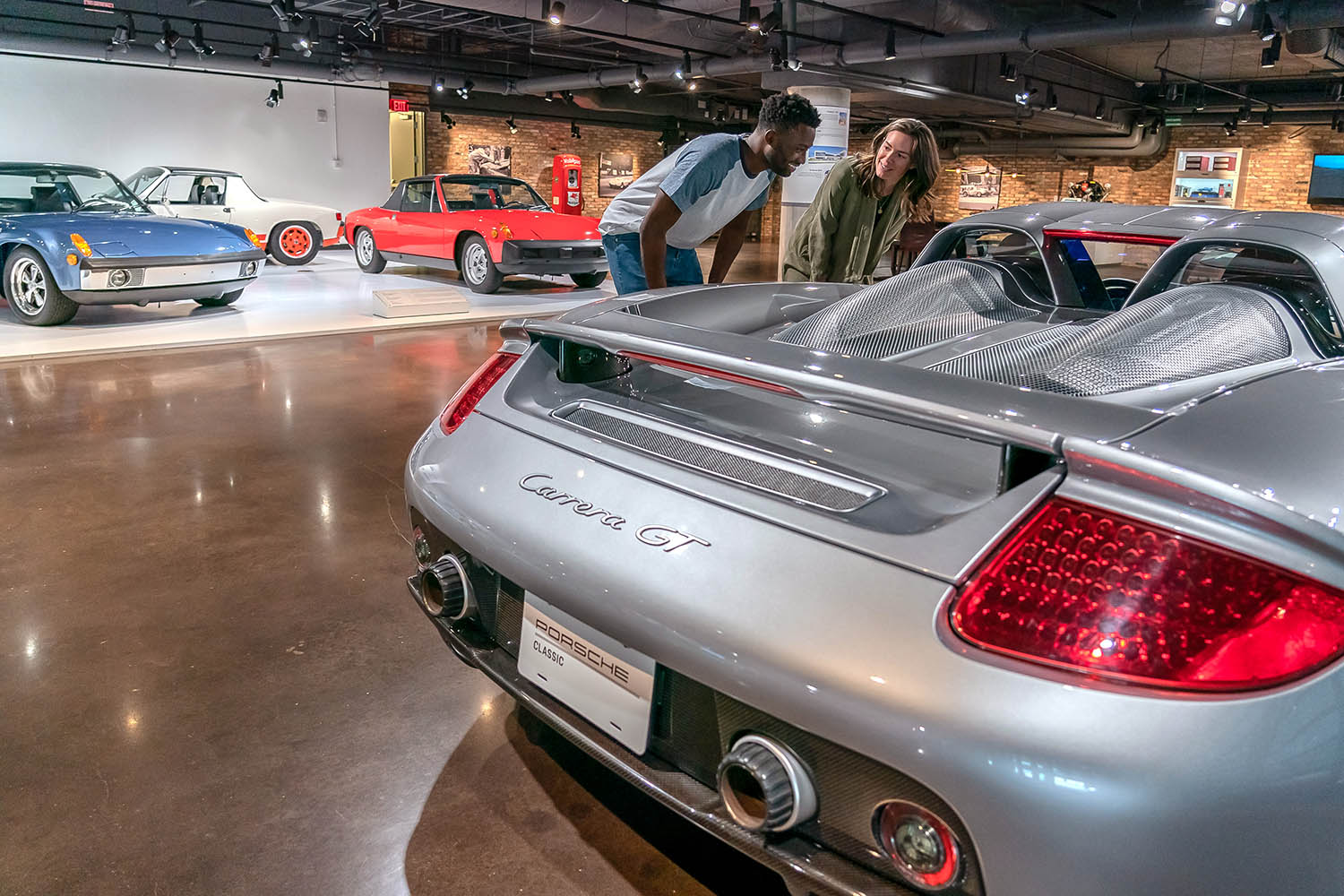 Two people inside the Porsche Experience Center in Atlanta, Georgia, looking at a silver Carrera GT