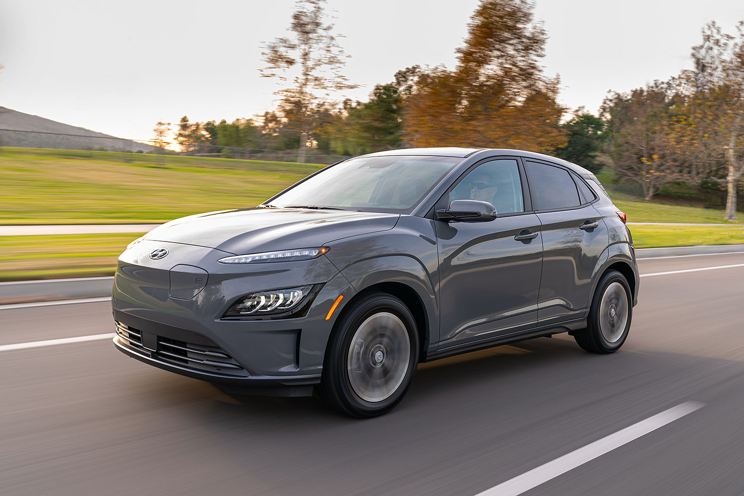 2023 Hyundai Kona Electric in gray driving along a tree-lined parkway