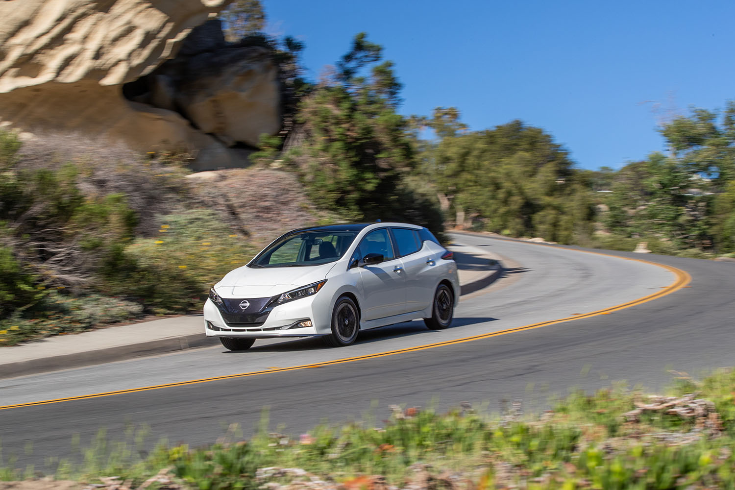 2023 Nissan Leaf in white rounding past a bend on a two-lane, mountainous road