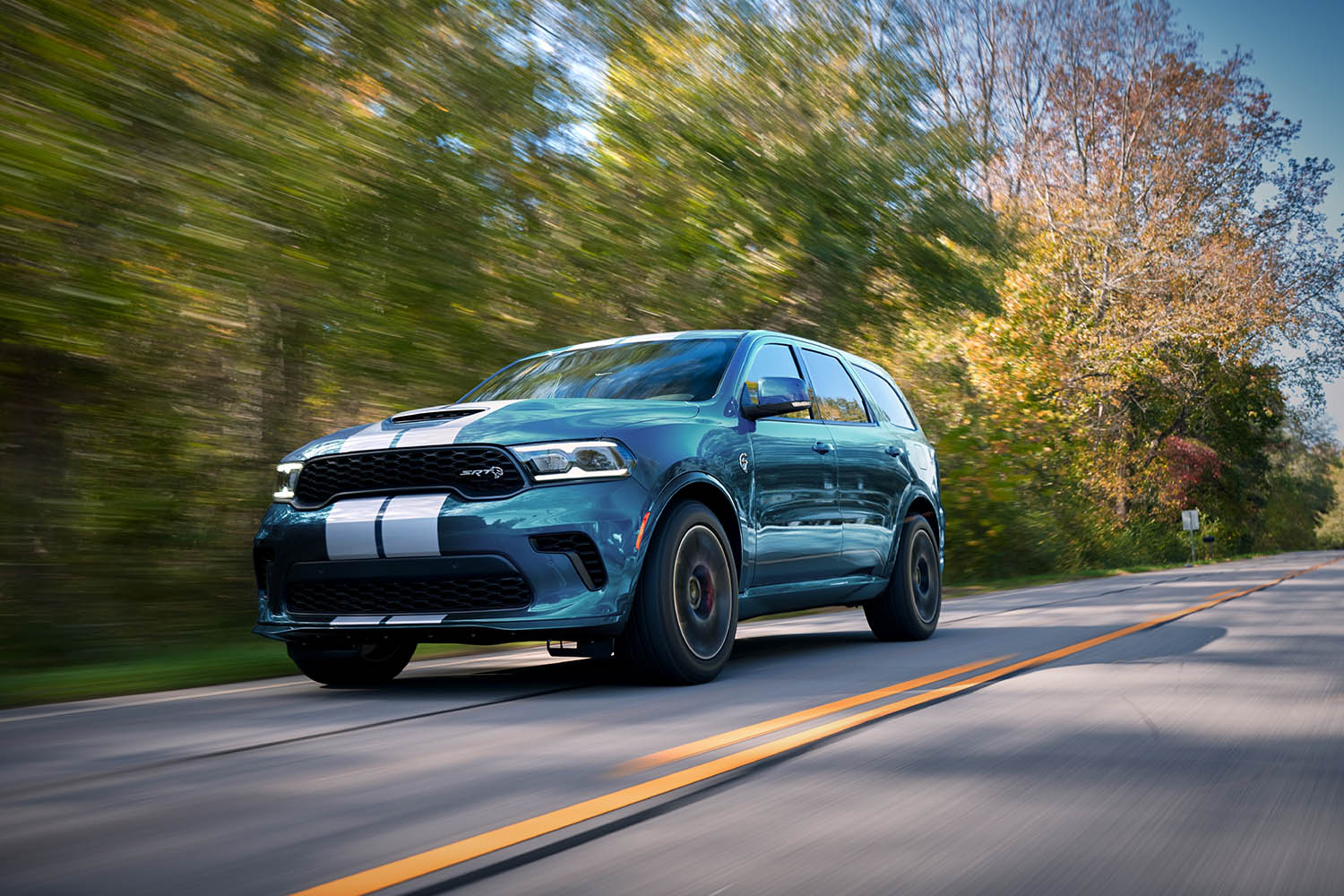 2023 Dodge Durango SRT Hellcat in blue with white stripes driving down a tree-lined, two lane road