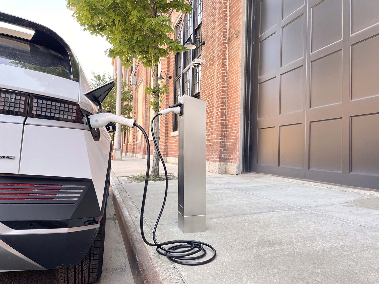 Electric vehicle in white parked at a curb and plugged into a charging station