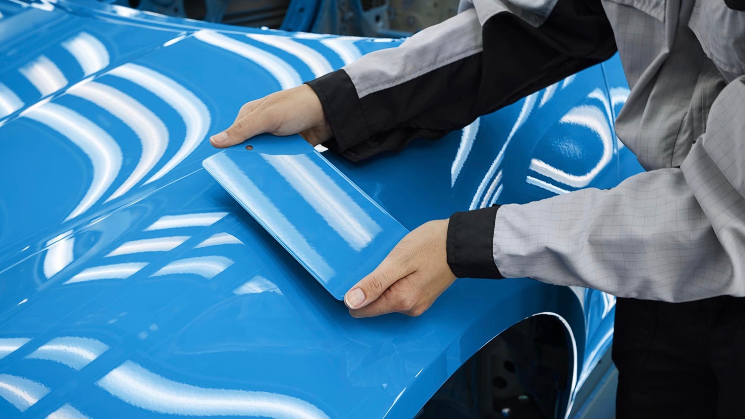 A person comparing a blue paint sample with the blue paint on a car body