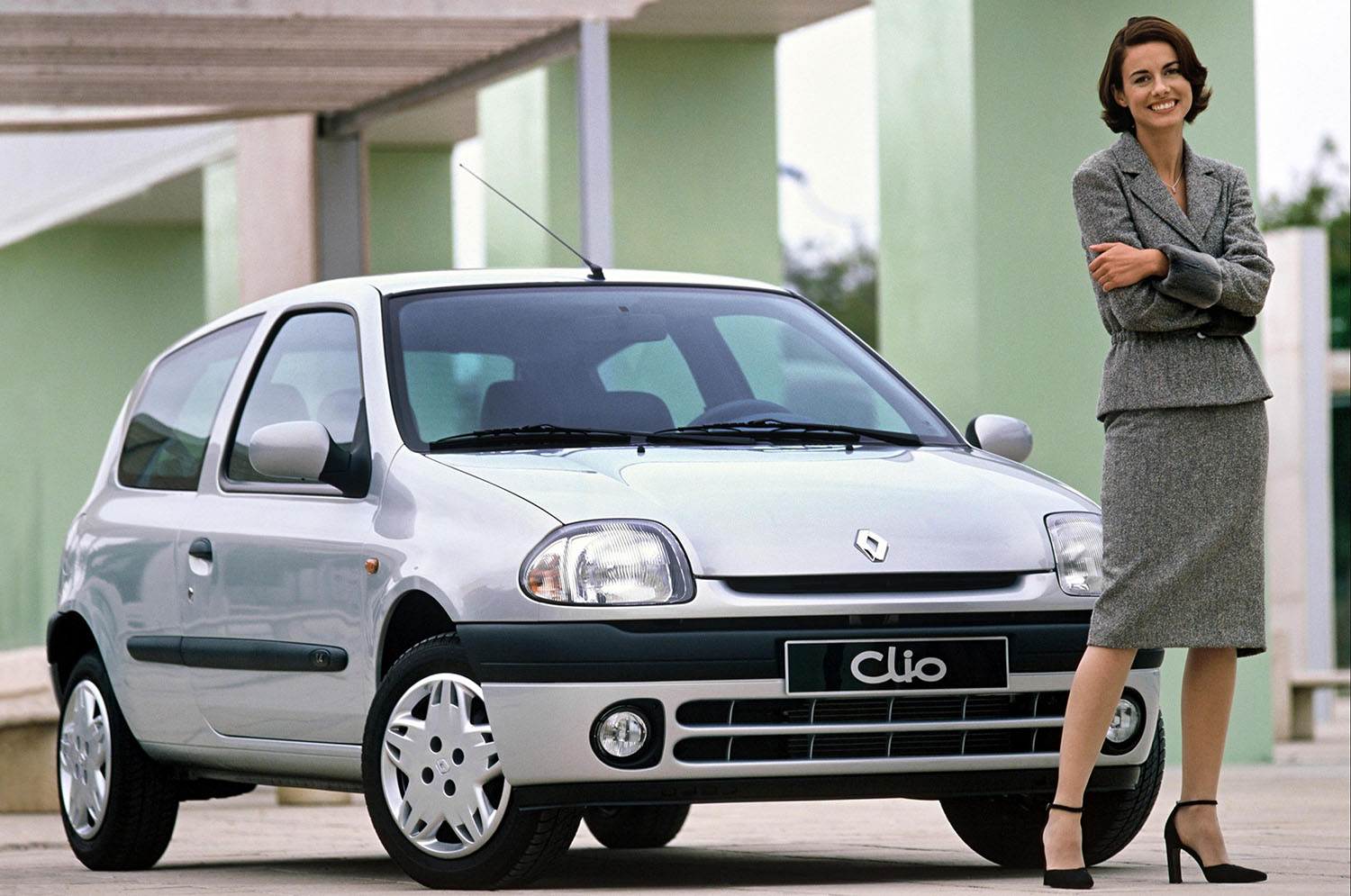 1990s-era Renault Clio Sport in silver with a smiling woman standing in front of it