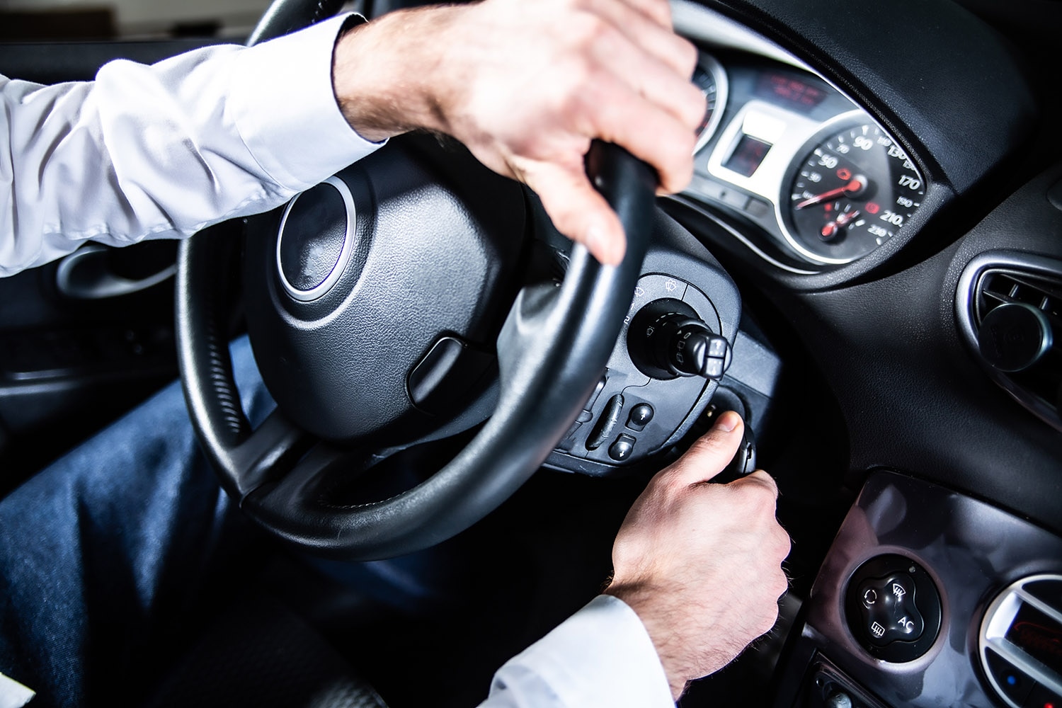 A driver's hands on the steering wheel and the ignition of a car