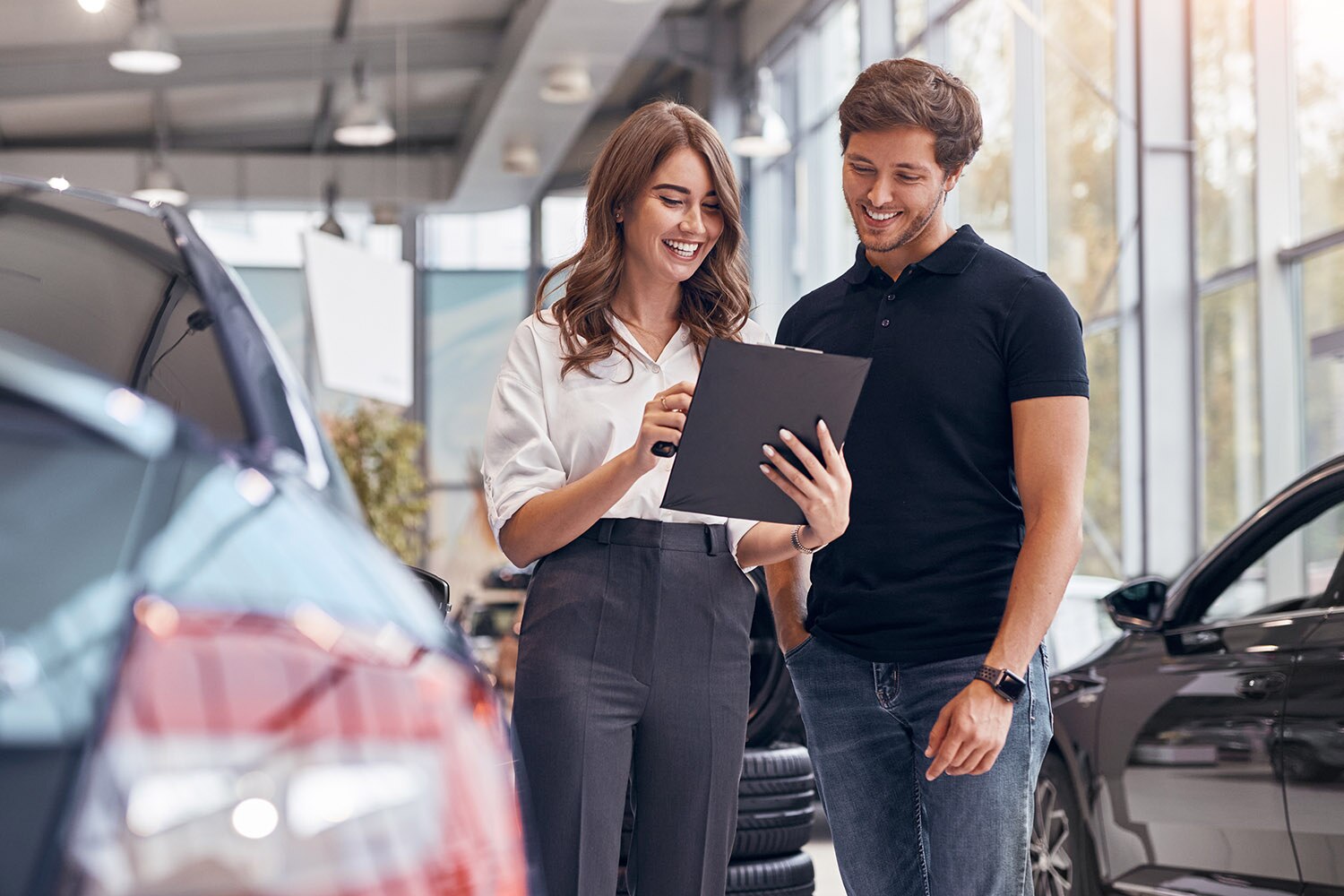 Woman explaining auto loan terms to man in car dealership showroom