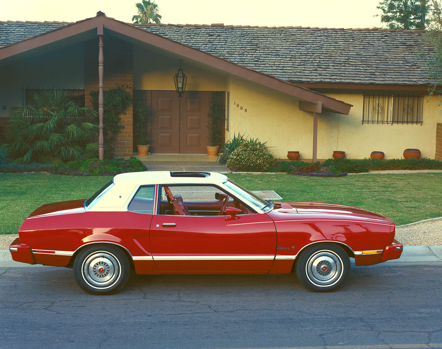 1974 Ford Mustang II in red with a white landau roof parked in front of a house