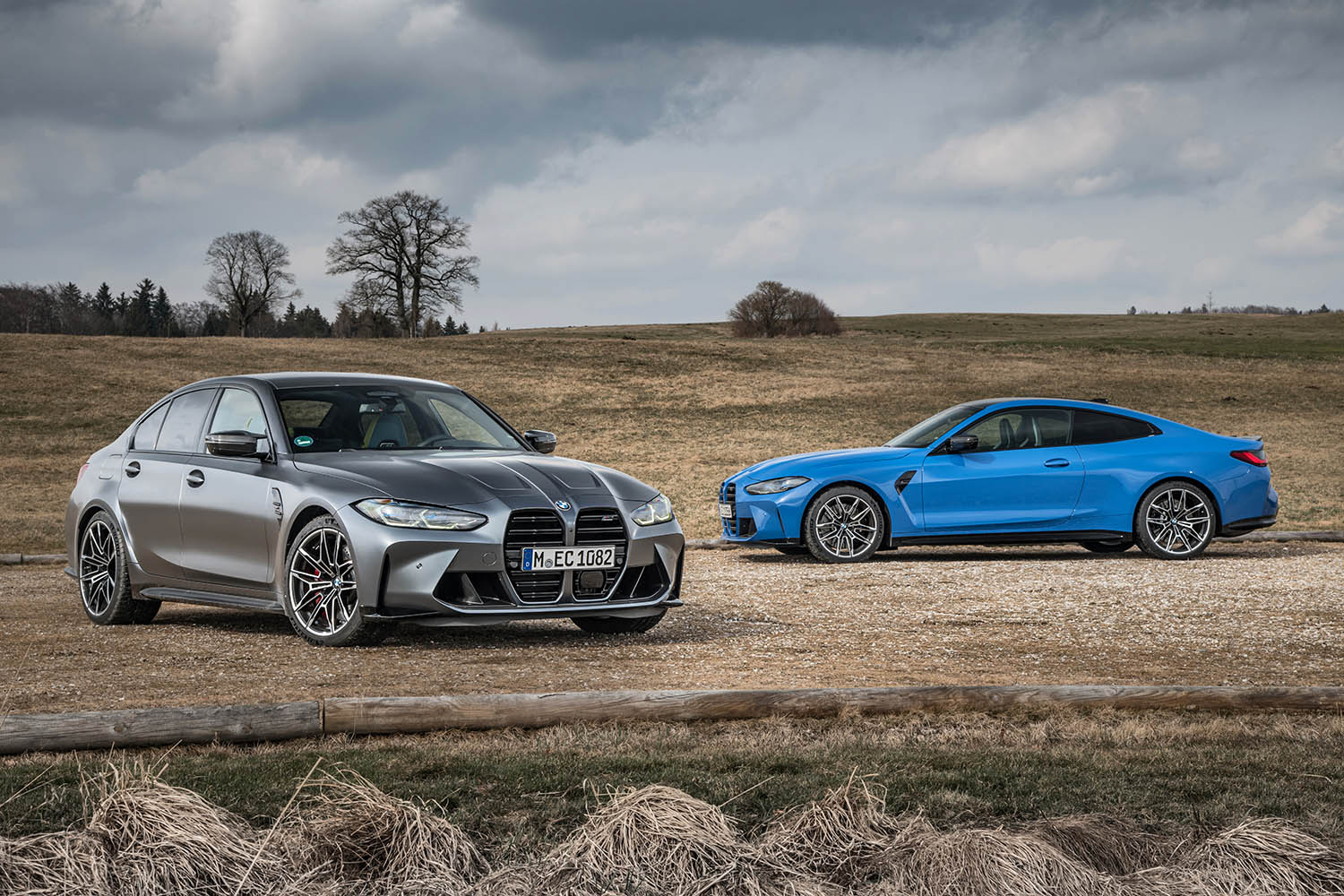 BMW M3 Sedan in gray and a BMW M4 Coupe in blue parked in an open field