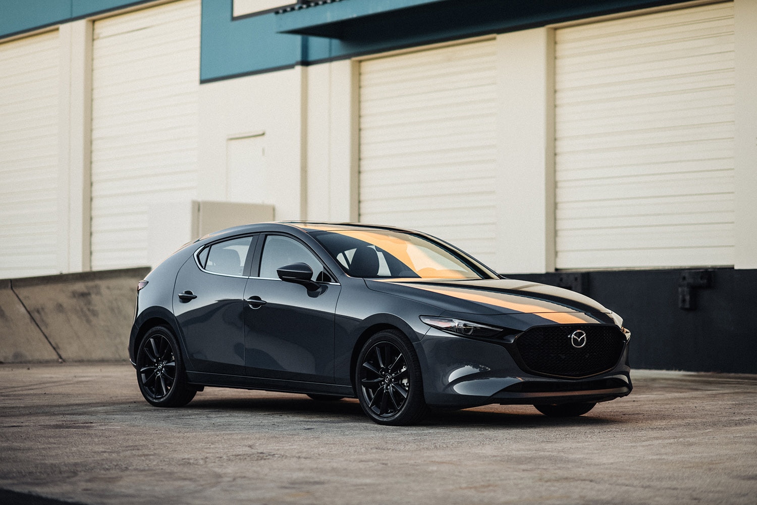 2023 Mazda 3 hatchback in dark gray parked in front of a warehouse