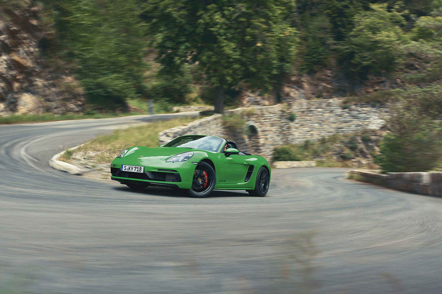 Porsche 718 Boxster GTS 4.0 in green about to reach the apex of a sharp bend along a serpentine alpine road