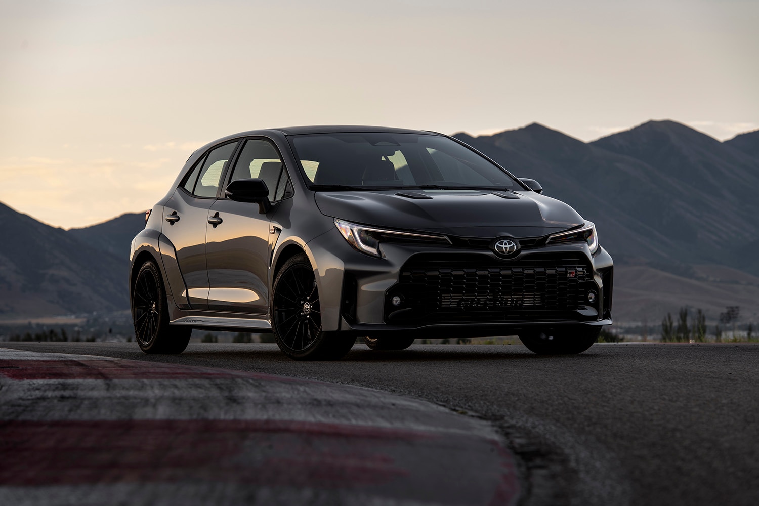 2023 Toyota GR Corolla Circuit Edition painted in Heavy Metal (dark gray) and parked near a racetrack corner apex