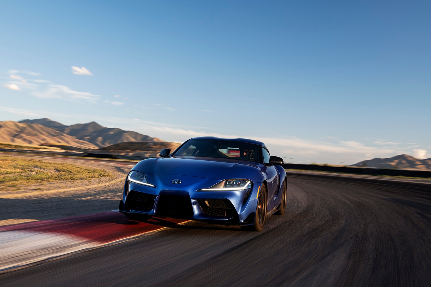 2023 Toyota GR Supra 3.0 Premium in Stratosphere blue hugging the inside curb of a desert racetrack's long sweeper