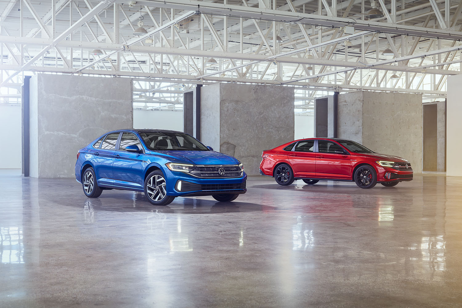 2023 Volkswagen Jetta in blue and Jetta GLI in red parked inside a building with a museum gallery-like interior