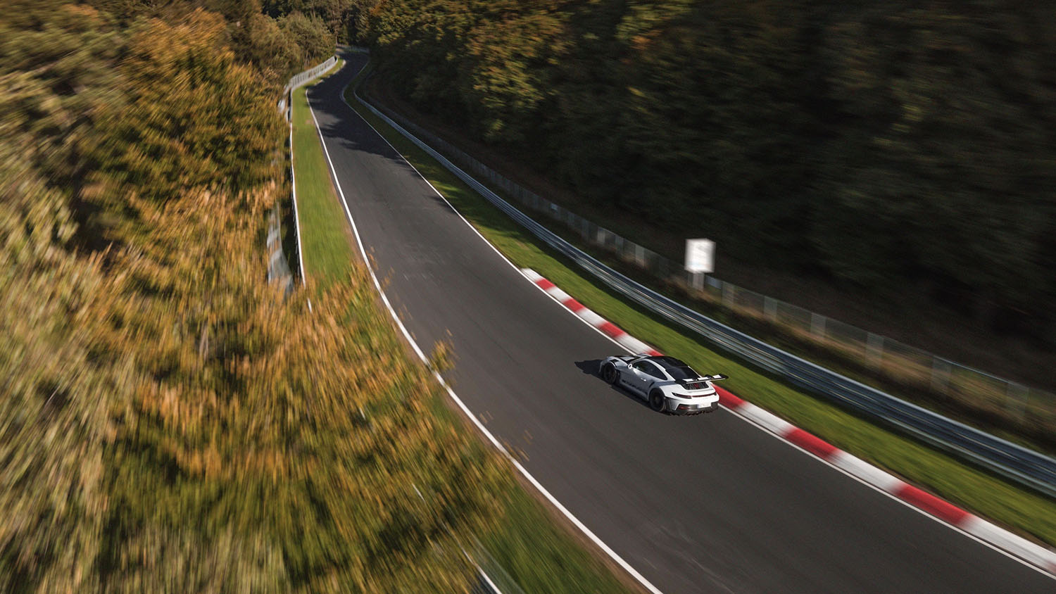 Long-distance three-quarters shot of a Porsche 911 GT3 RS driving on the Nundefinedrburgring