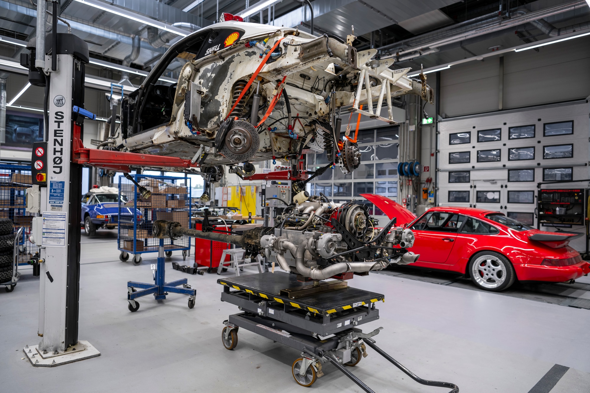 Engine being reinstalled in the 959 Paris-Dakar next to a red Porsche inside the Porsche Classic workshop