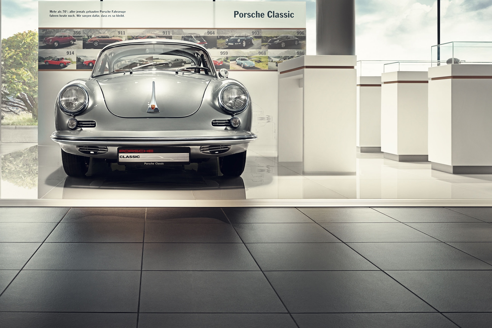 Alt Text: Silver Porsche 356 in showroom in front of a Porsche Classic banner in 2016