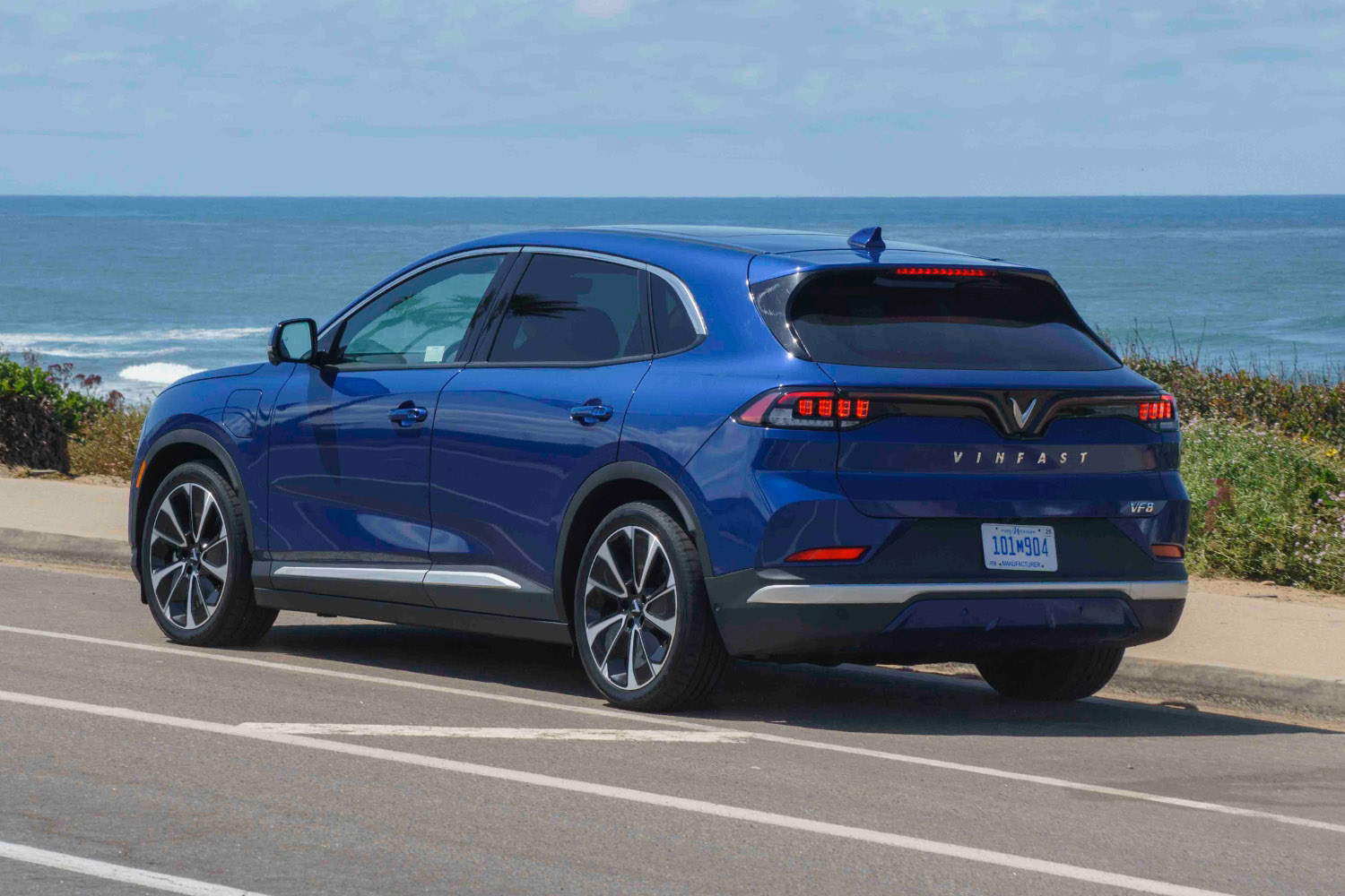 : 2023 Vinfast VF 8 in blue parked along the side of a beachside road, rear three-quarter angle