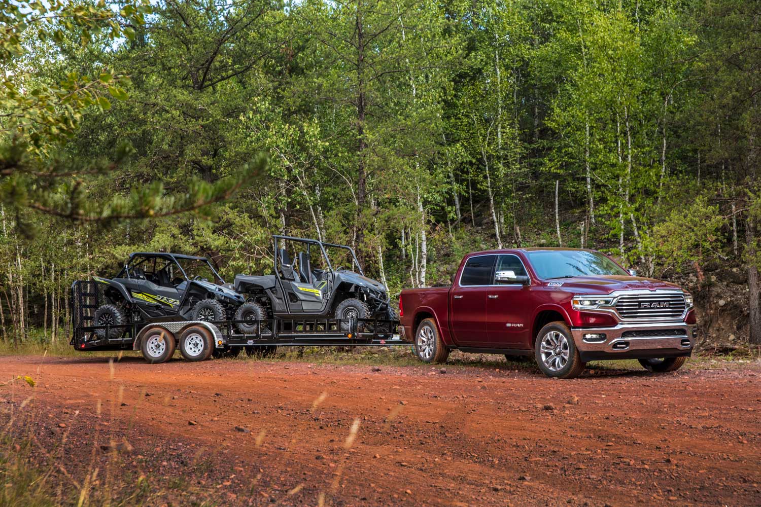 2023 Ram 1500 in red towing trailer with two off-road vehicles (side-by-sides) loaded