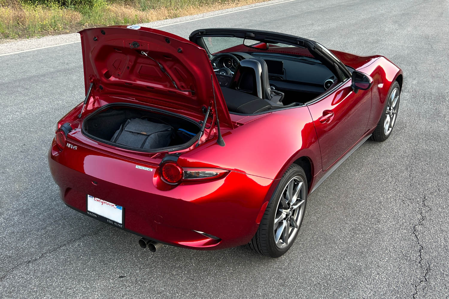 2023 Mazda MX-5 Miata stopped on a country road with its trunk lid open and an overnight bag inside
