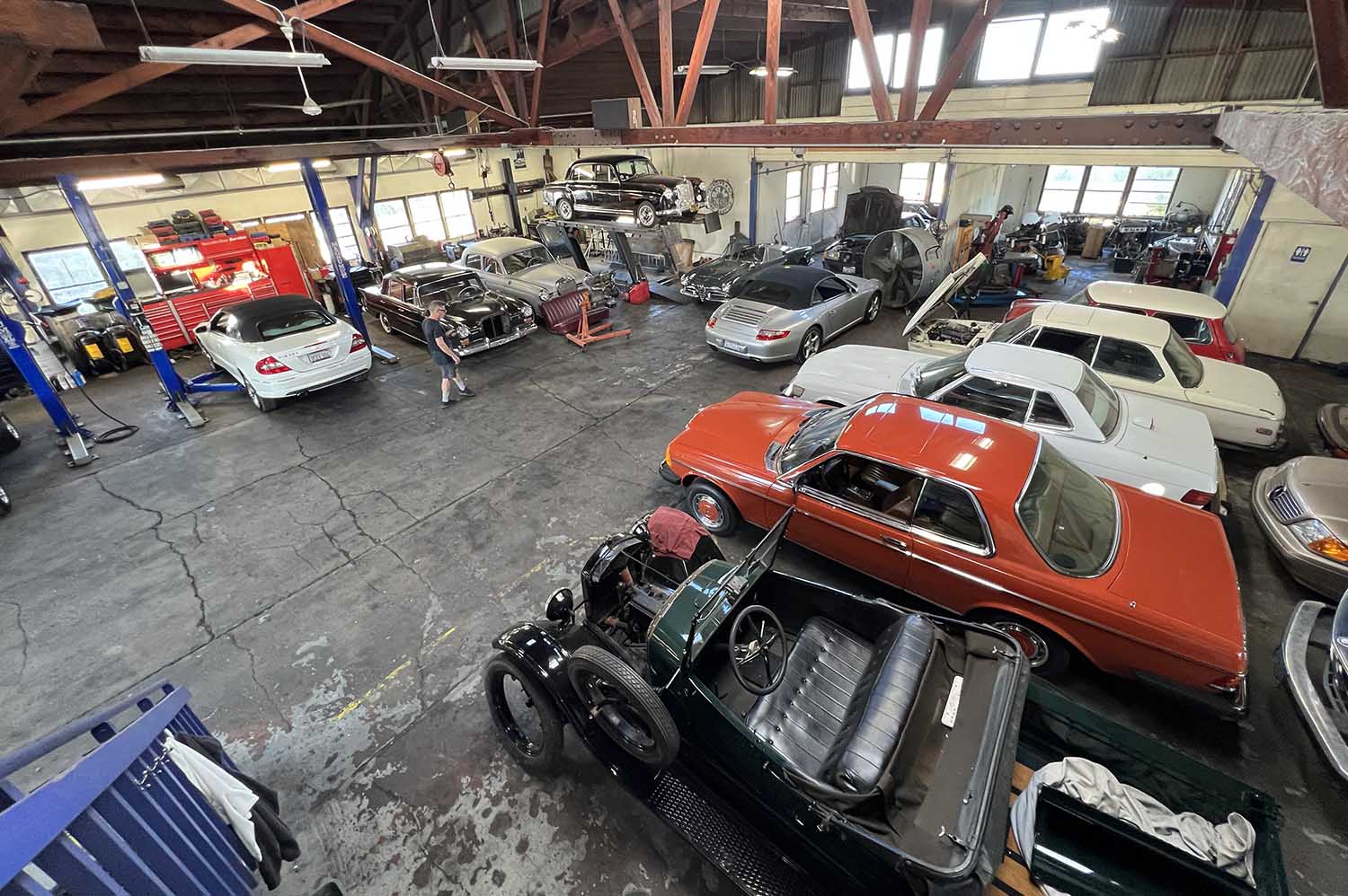 A variety of classic cars sits in an auto-repair shop