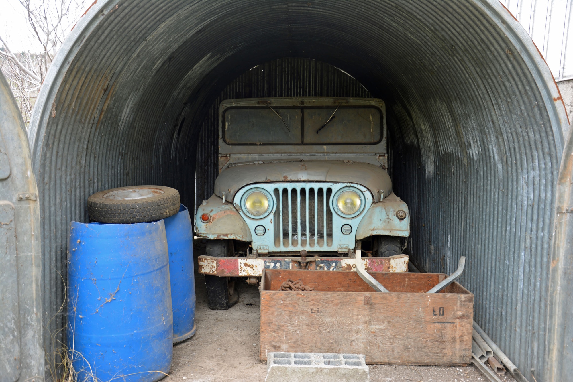 Old blue Jeep M38 parked in a shed with old junk
