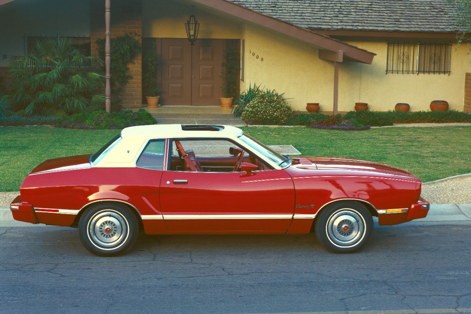 1974 Ford Mustang II in red with a white landau roof parked in front of a house