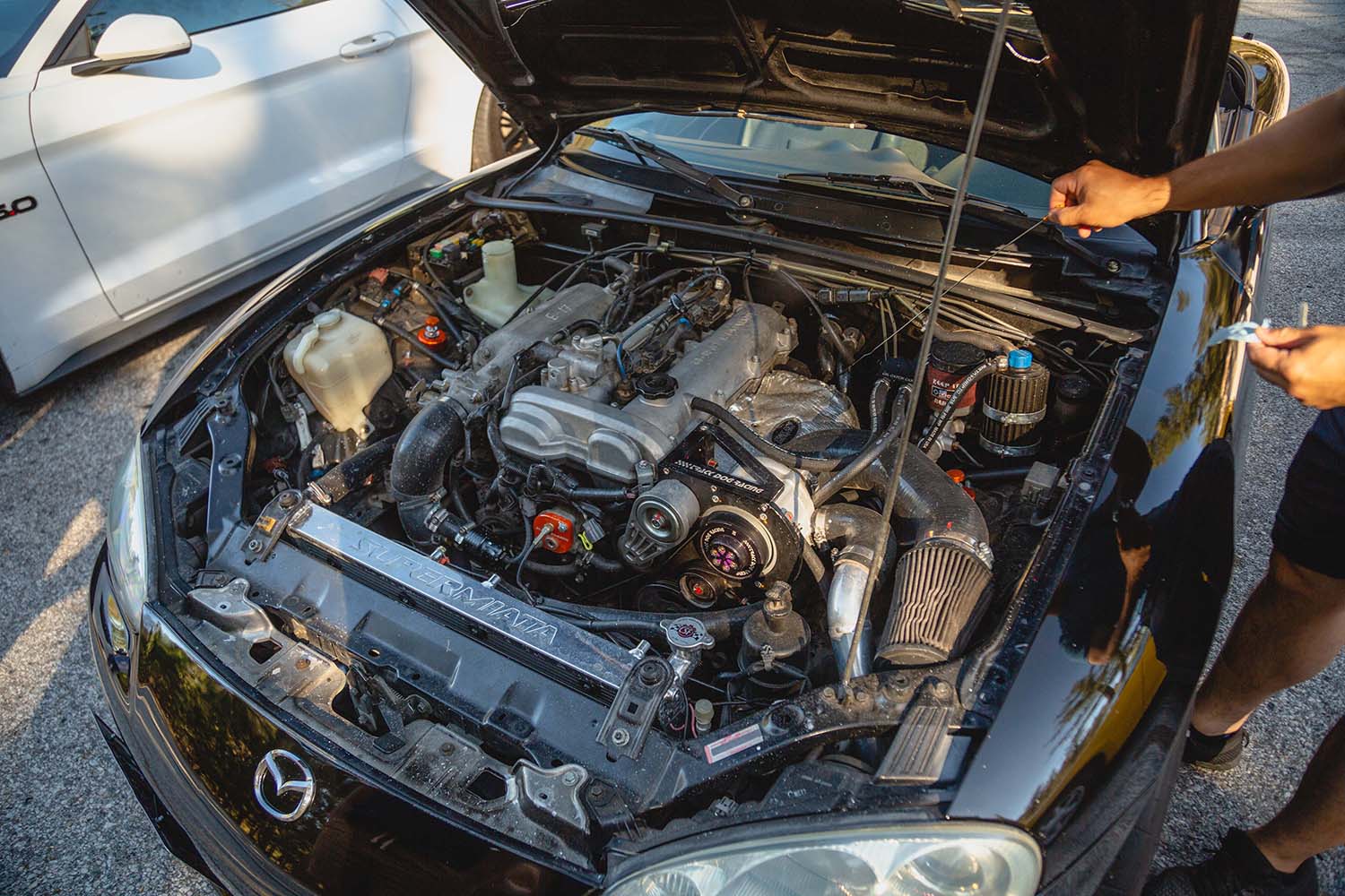 View under the hood of a Mazda vehicle with a person checking the engine oil